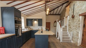 Une cuisine spacieuse avec des meubles de couleur sombre, un îlot central et un mur en pierre.