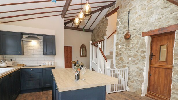 Une cuisine avec des meubles de couleur sombre, un îlot central en bois et un mur en pierre.