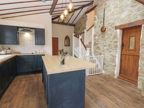 A kitchen with dark cabinets, a wooden island, and a stone wall. - Parkers House (Alston)