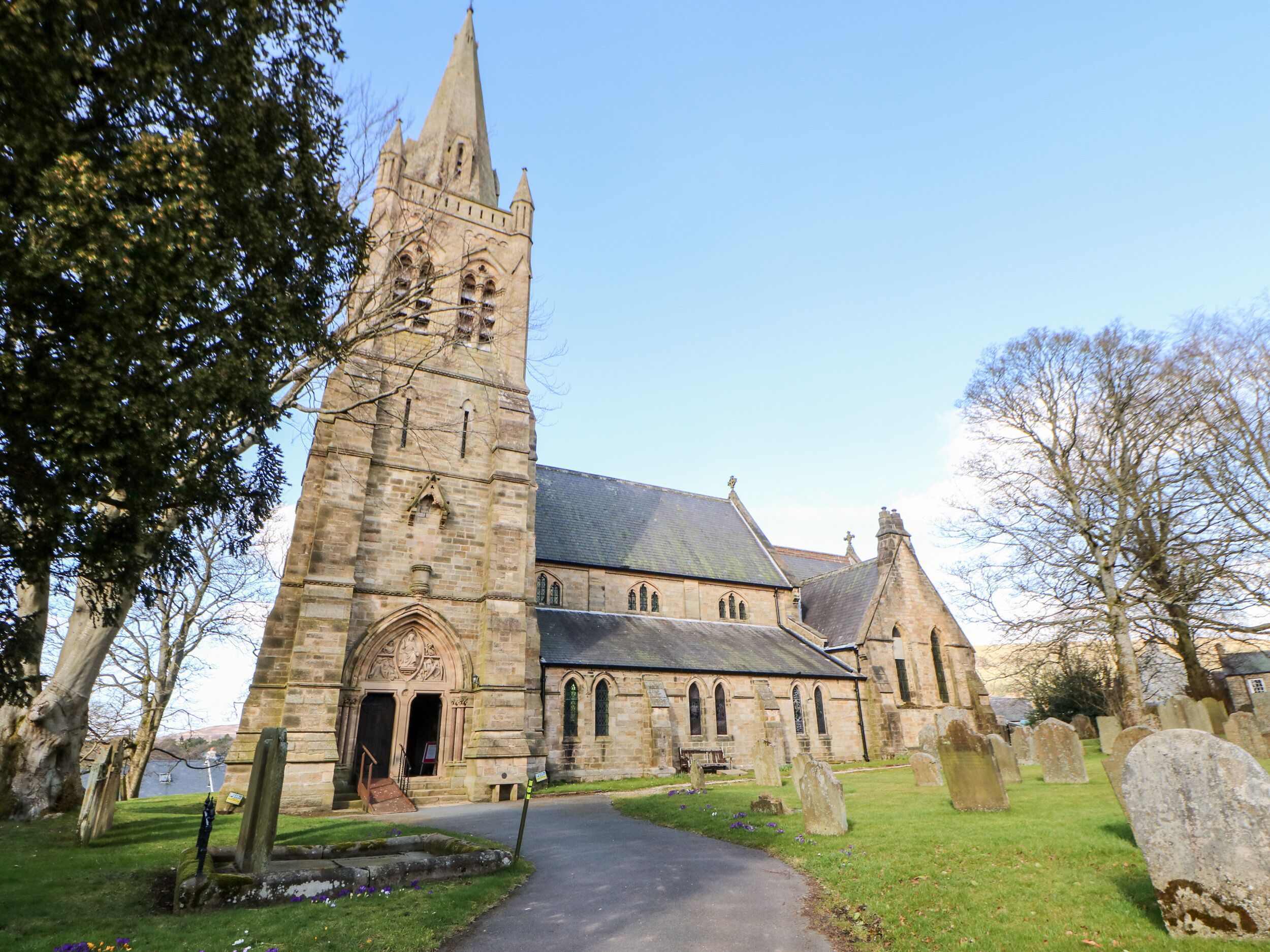 A church with a tall tower, a main building with arched windows, and a graveyard with headstones.