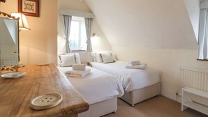 A bedroom with two beds, a wooden table, a mirror, and a window with curtains.