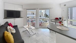 A modern living room with a sofa, a coffee table, a TV mounted on the wall, and a balcony with a view of the city. - Cannes: Pointe croisette 1 bdr apartment 100 m to beaches - cute balcony (Cannes)