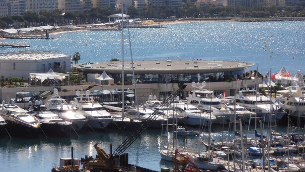 A marina with numerous yachts docked, a modern building with a circular roof, and a cityscape in the background. - Cannes: Pointe croisette 1 bdr apartment 100 m to beaches - cute balcony (Cannes)