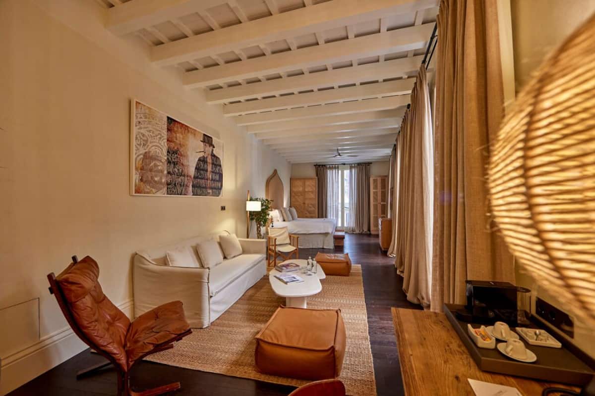 Een moderne hotelkamer met een bank, fauteuil, bijzettafeltje en een eethoek met een dienblad.