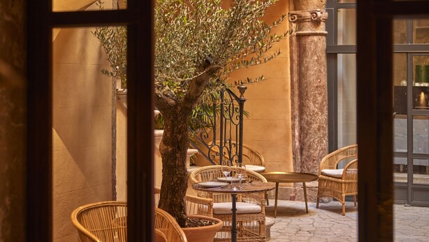 Un espace extérieur aménagé avec des meubles en osier, un arbre et un mur en pierre.