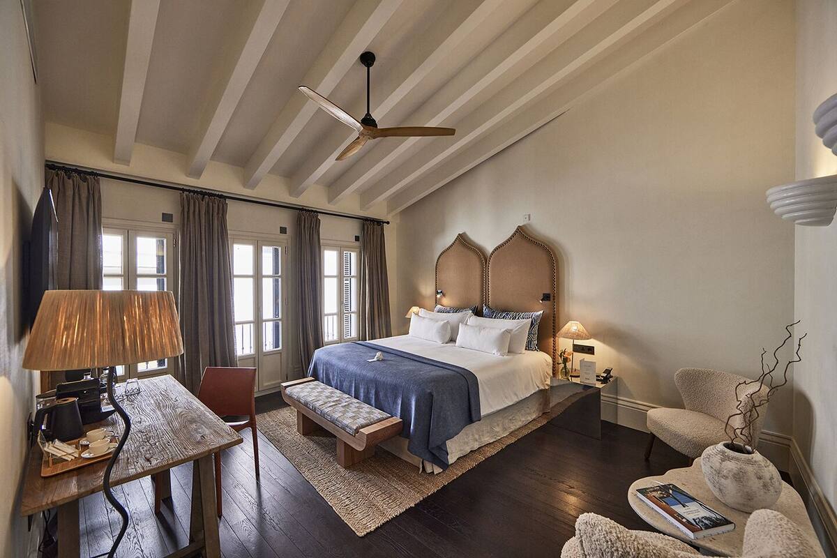 Hotelkamer met een groot bed, een bureau met lamp, een stoel, een klein tafeltje en een decoratieve vaas.