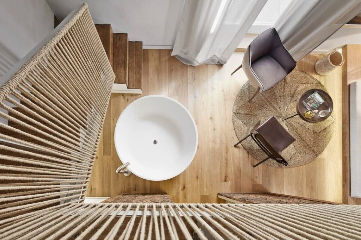 Een modern interieur met een rond wit bad, een houten vloer en een zithoek met een ronde tafel en een stoel.