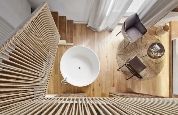 Un interior moderno con una bañera redonda blanca, suelo de madera y un área de descanso con una mesa redonda y una silla.