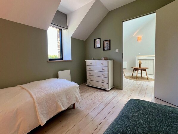 A bedroom with a bed, dresser, and a view of a dining area.