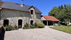 A stone farmhouse with a gravel driveway, a chimney, and a red-roofed outbuilding.