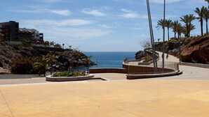 Une place dallée avec un espace de repos circulaire, un lampadaire et une vue sur la mer.