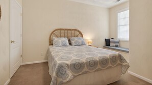 A bedroom with a bed, a window with blinds, a bedside table, and a wall-mounted light.
