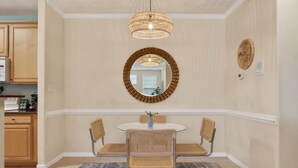 A dining area with a round table, four wicker chairs, a woven pendant light, a mirror, and a wall-mounted decorative plate.