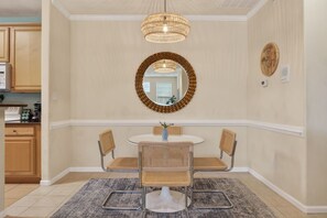 Uma sala de jantar com uma mesa redonda, quatro cadeiras de vime, uma luminária pendente trançada, um espelho e um prato decorativo na parede.