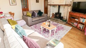 A cozy living room with a sofa, coffee table, and a fireplace. - Healey Farm Cottage (Morpeth)