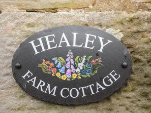 Kivestä valmistettu kyltti, jossa on teksti ”HEALEY FARM COTTAGE” ja koristeellinen kukka-aihe.