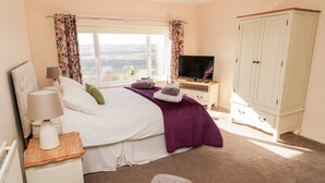A bedroom with a bed, a TV, a wardrobe, a nightstand, and a window with curtains. - Healey Farm Cottage (Morpeth)