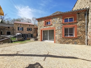 A stone building with a red-tiled roof, a large sliding glass door, and a gravel driveway. - Charming Retreat with Sauna and Terrace in Peaceful Hamaulet (Saint-Just-prés-Brioude)