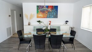 Un comedor moderno con una mesa de vidrio, sillas negras y un cuadro abstracto colorido en la pared.