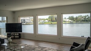 Sala de estar com uma TV grande, uma mesa de centro e vista para um lago com casas ao fundo.