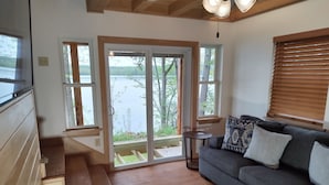 Ein gemütliches Wohnzimmer mit grauem Sofa, einer Holztreppe und großen Schiebegläsern, die auf einen Balkon mit Seeblick führen.