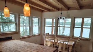 Ein Essbereich mit Holztisch und Stühlen, großen Fenstern mit Seeblick und hängenden Pendelleuchten.
