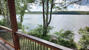 Eine Holzterrasse mit Geländer, die auf einen See blickt, umgeben von Bäumen und Grün.