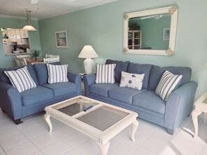 A living room with two blue sofas, a glass coffee table, a white lamp, and a mirror on the wall. - Ocean view 2 bedroom, 2.5 bath townhouse. (St. Augustine)