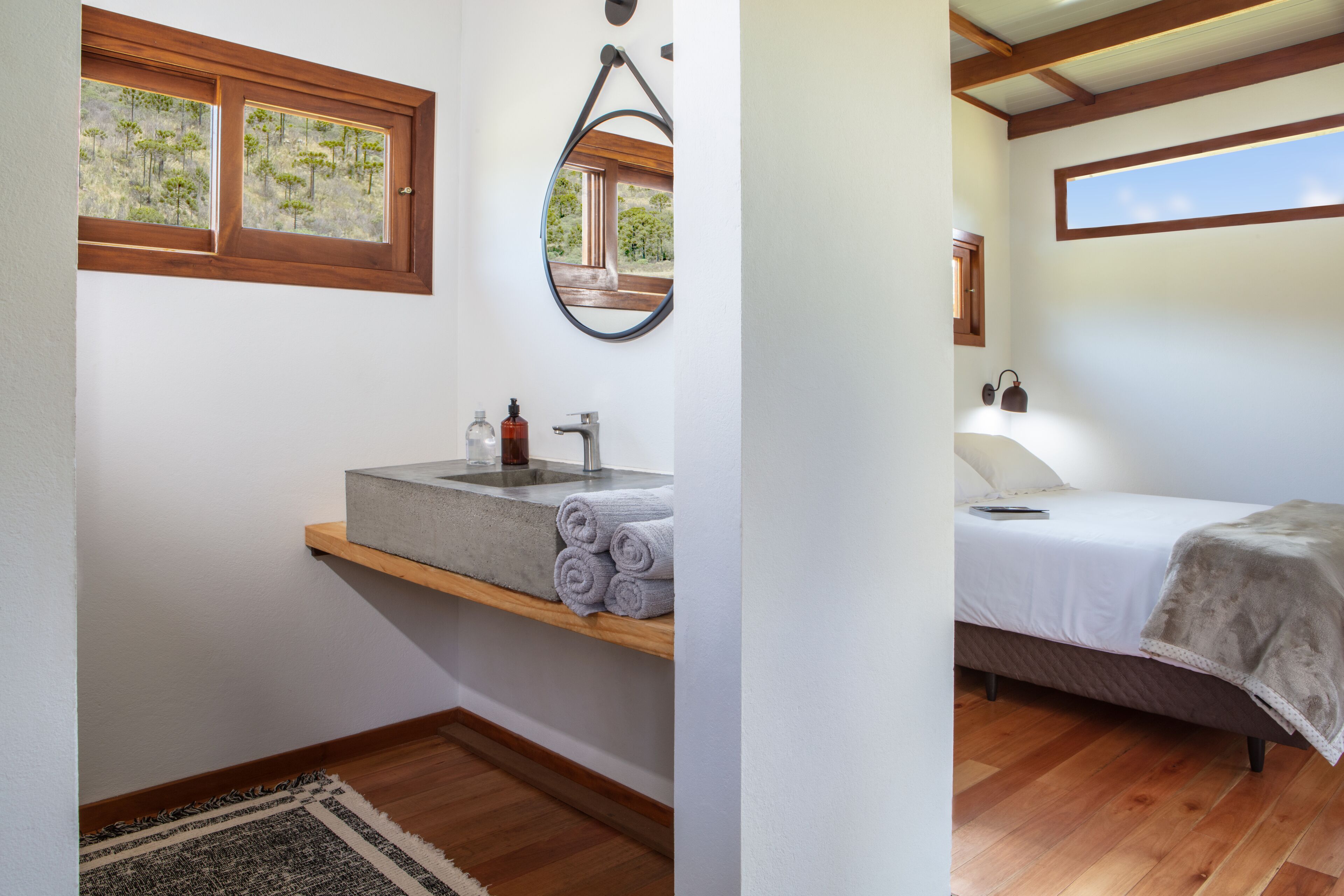 Une chambre à coucher comprenant un lit, une table de chevet, une fenêtre, un miroir et une salle de bain avec un lavabo et un porte-serviettes.
