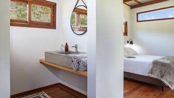 Une chambre à coucher comprenant un lit, une table de chevet, une fenêtre, un miroir et une salle de bain avec un lavabo et un porte-serviettes.