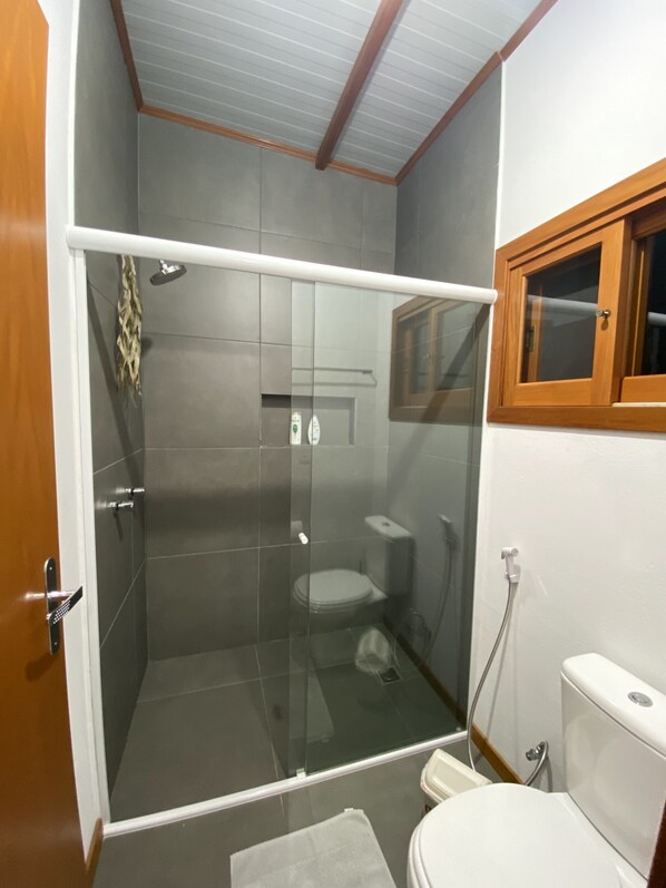 Un baño con ducha envuelta en vidrio, inodoro y ventana con marco de madera.