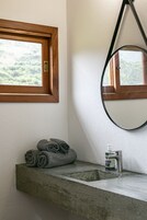 Un baño con un lavamanos de hormigón, una ventana con marco de madera y un espejo.