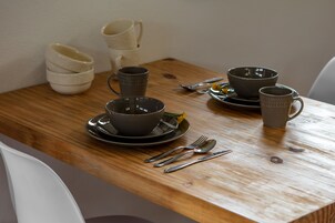 Una mesa de madera con varios cuencos y tazas, algunas apiladas, y un par de tenedores y cucharas sobre la mesa.