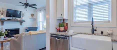 A modern kitchen with white cabinetry, a built-in dishwasher, and a window with blinds.