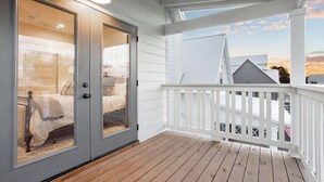 A covered porch with a white railing, a glass door leading to a bedroom with a bed and a nightstand, and a view of a house in the background. - My Happy Place at River Rocks Plantation (Guntersville)