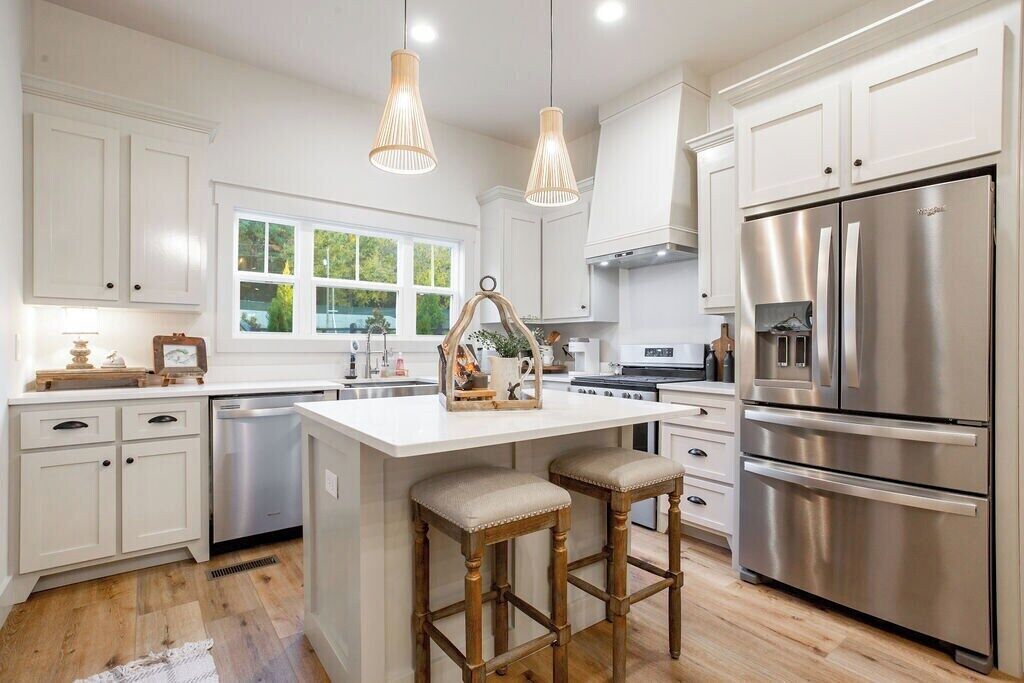 Una cocina moderna con armarios blancos, electrodomésticos de acero inoxidable y una isla central con taburetes.