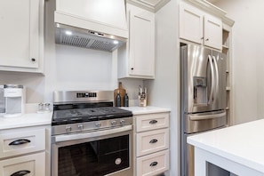 A kitchen with a stainless steel stove, oven, and refrigerator, white cabinetry, and a coffee maker.