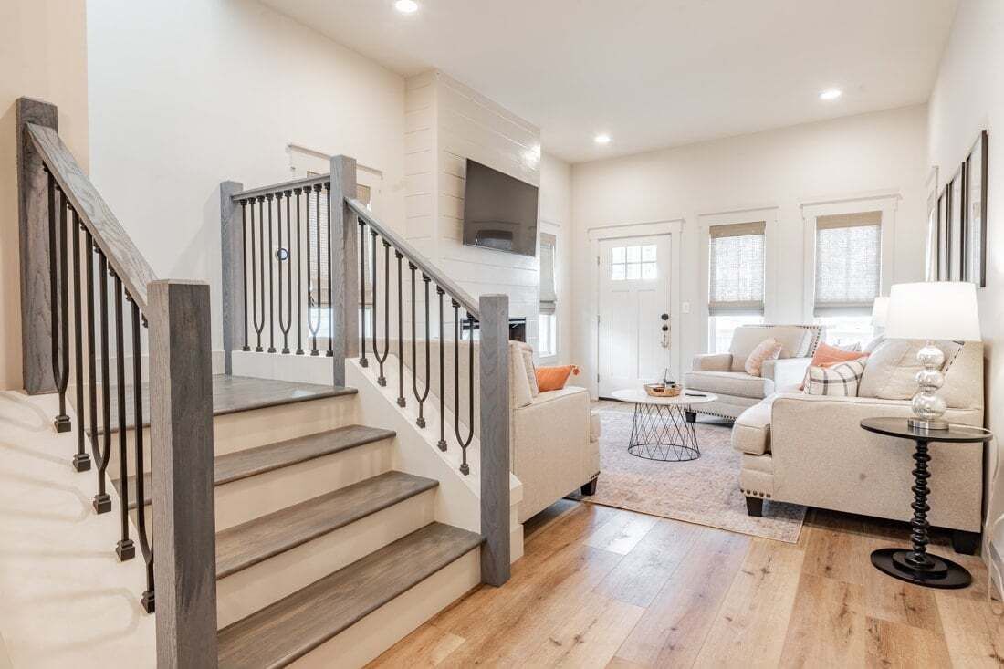 A staircase with wooden steps and metal railings leading to a living area with a sofa, a coffee table, and a TV mounted on the wall.