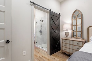 A bedroom with a sliding door leading to a shower area, a bedside table with a lamp, and a mirror.