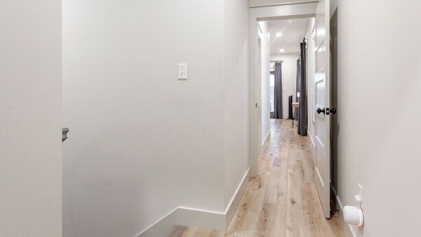 A narrow hallway with white walls and wooden flooring, leading to a door with a black handle. - My Happy Place at River Rocks Plantation (Guntersville)