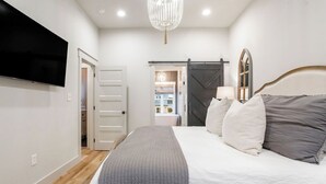 A bedroom with a bed, a chandelier, a TV, and a sliding door. - My Happy Place at River Rocks Plantation (Guntersville)