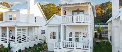 A white two-story house with a balcony, a front porch, and a small front yard.