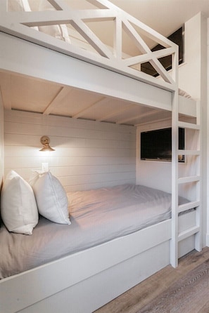 Uma cama beliche com escada, uma luminária de cabeceira e uma janela.