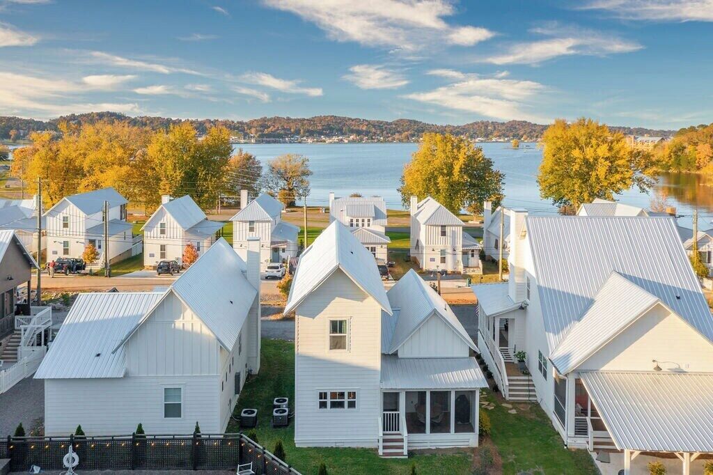 A cluster of white buildings with pitched roofs, a lake, and autumn foliage in the background.
