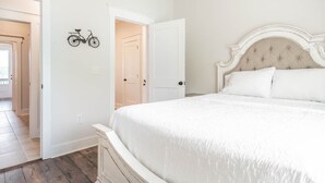 A bedroom with a white bed, a bicycle wall art, and a door leading to another room.