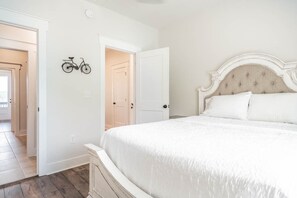 A bedroom with a white bed, a bicycle wall art, and a door leading to another room.