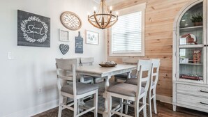 A dining area with a white table and chairs, a chandelier, and wall decorations including a heart and a circular piece with text.