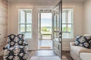 A room with two armchairs, a sofa, a door leading outside, and a view of a deck.