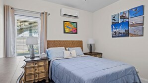 Un dormitorio con cama, mesitas de noche, una ventana con cortinas, aire acondicionado y decoración en la pared.
