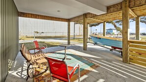 Un espacio al aire libre techado con un banco y una mesa de madera, vista a un barco azul y un muro de metal corrugado.